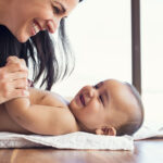 Happy mother playing with baby while changing his diaper. Smilin