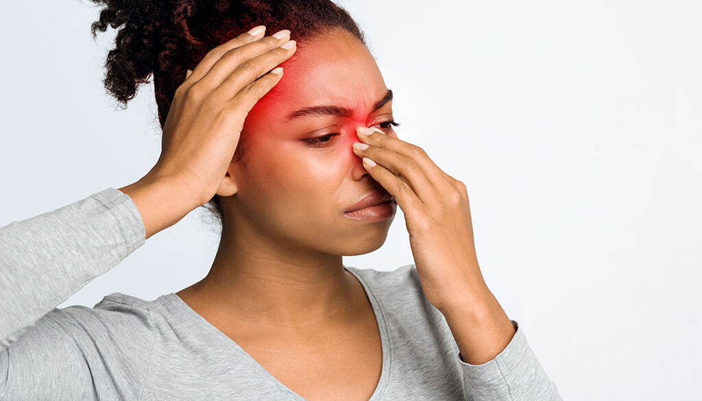 An African American Woman Holding Her Nose and Head That Are Highlighted in Red Can Chronic Sinusitis Affect Your Whole Body