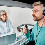 A Male Patient Sitting With an Audiologist Wearing Headphones & Holding a Response Button During a Hearing Test Types of Hearing Test