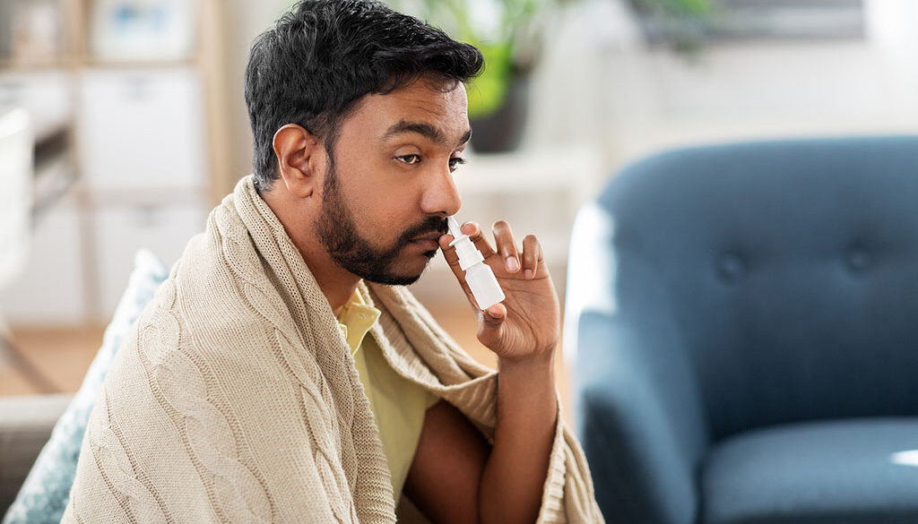 A Man Sitting on His Couch Wrapped in a Blanket Using Nasal Spray to Clear His Nose Can Nasal Spray Cause Loss of Smell