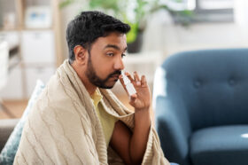 A Man Sitting on His Couch Wrapped in a Blanket Using Nasal Spray to Clear His Nose Can Nasal Spray Cause Loss of Smell