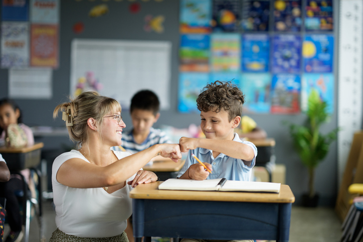 A teacher and student engage positively in a classroom setting, fostering learning and motivation. The interaction shows educational guidance and support in a diverse and colorful learning environment.